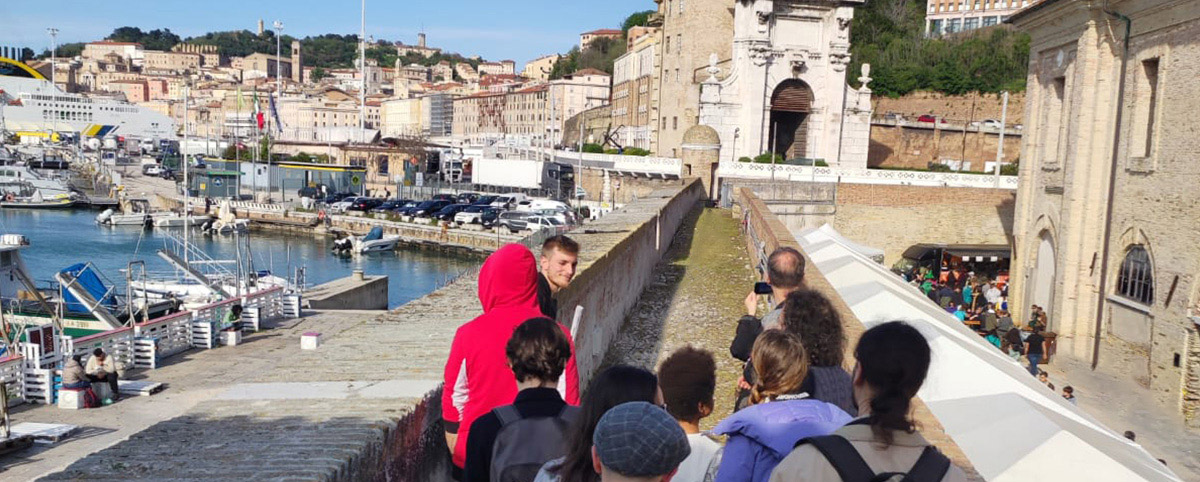 gruppo di visitatori con la guida sui camminamenti. Dietro il mare e un torrione d'angolo