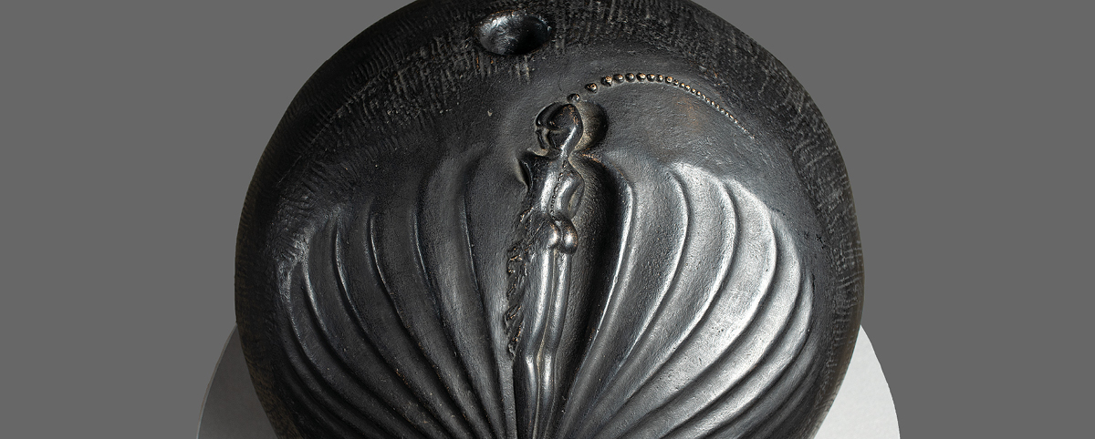 Porzione dell'opera "L'ombra vede" di Enzo Cucchi: il corpo di una donna visto da dietro, scolpito in una sfera di bronzo. La donna ha una lunga treccia di capelli.
